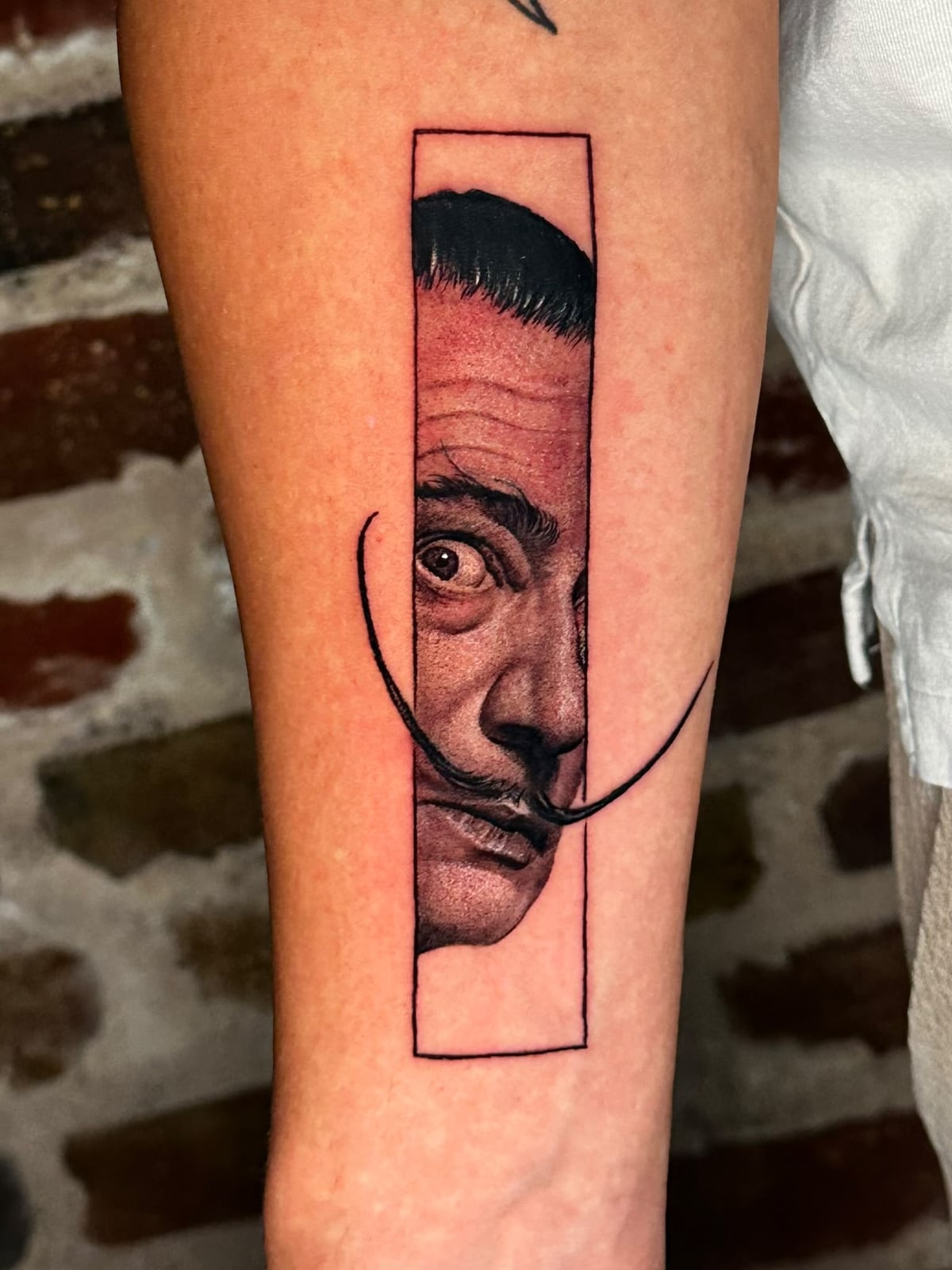 Tattoo: Dalí-Porträt im Rahmen am Unterarm