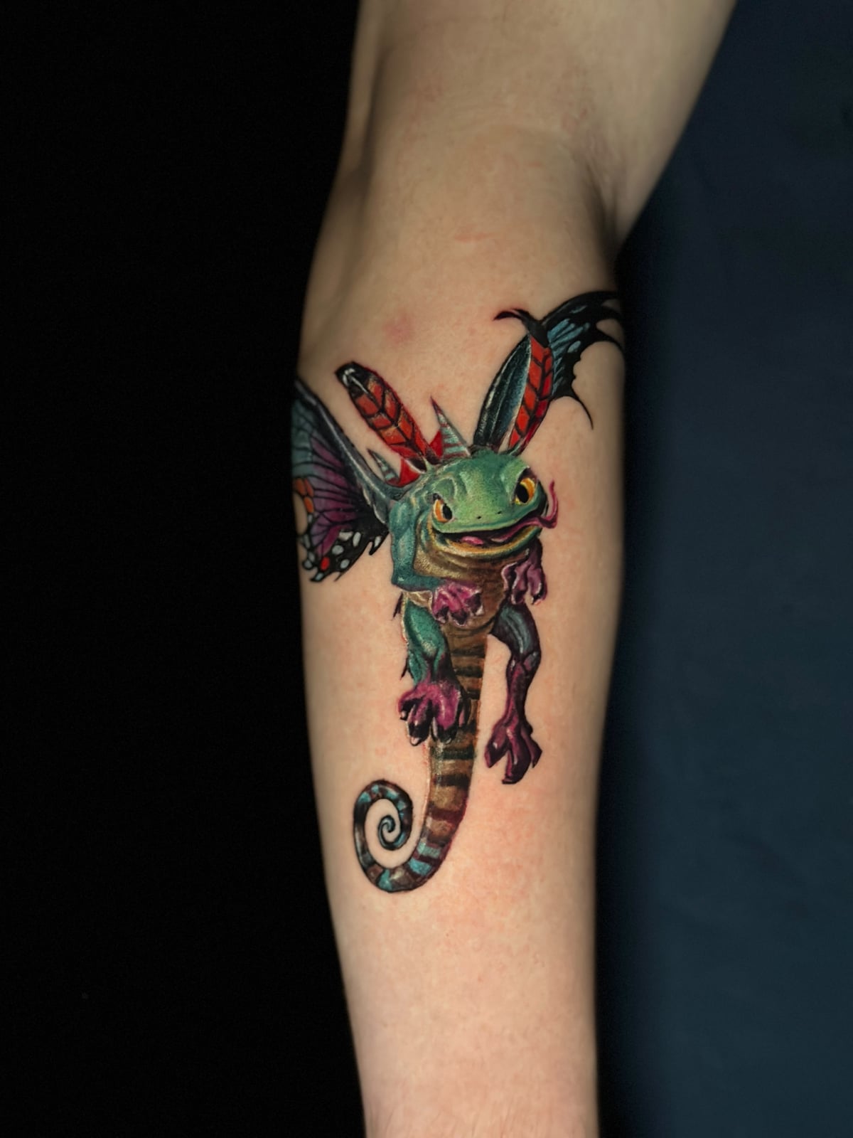 Tattoo: farbiges Fantasy-Wesen (Frosch mit Schmetterlingsflügeln) am Unterarm